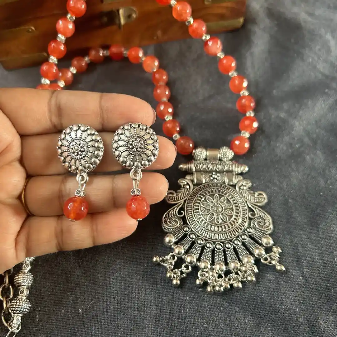 Handcrafted oxidised silver necklace and earring set featuring orange onyx beads and a large filigree floral pendant.