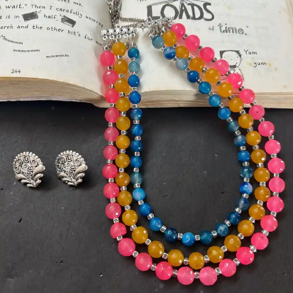 Multicolor bead necklace with pink, blue and yellow beads paired with oxidised silver stud earrings displayed on an open book background