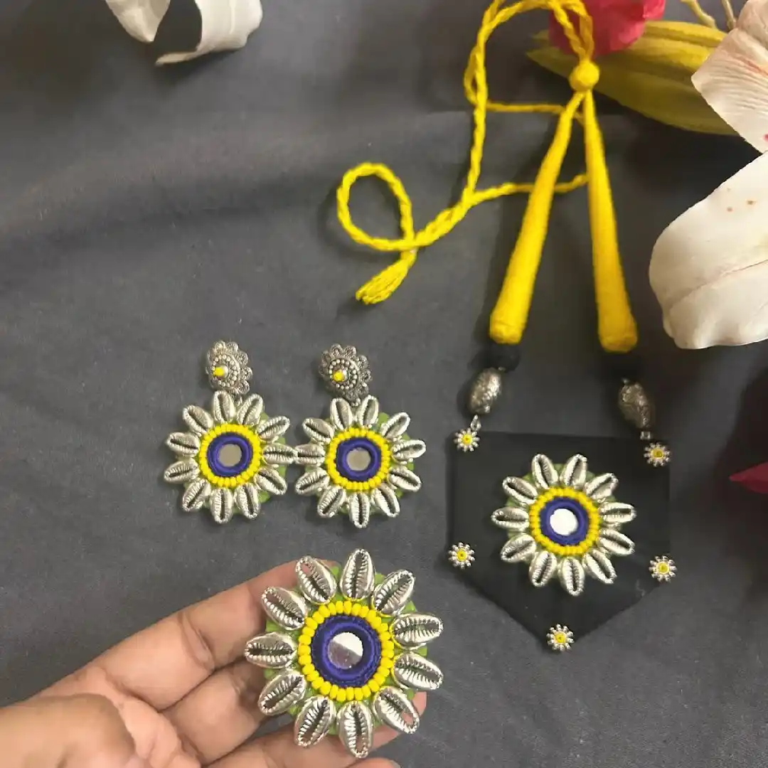 Handcrafted black fabric necklace and earring set from Itsy Bitzy Kolkata featuring yellow thread accents, floral mirror work, and silver-toned cowrie shell embellishments.