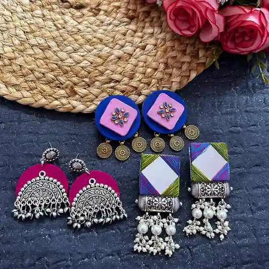 A collection of three pairs of handcrafted ethnic earrings featuring mirror work, pink and blue fabric designs, and oxidised silver with pearls.