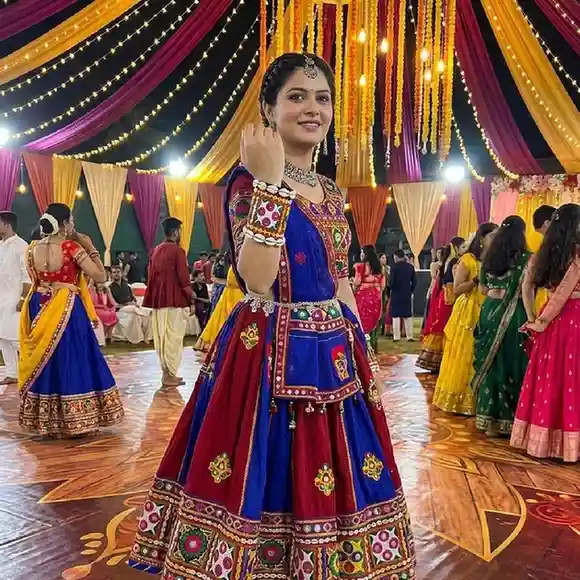 A model in a traditional colorful Navratri chaniya choli wearing a handcrafted Banjara-style fabric cuff with mirror work and cowrie shells, set against a festive background with Garba dancers and warm lighting
