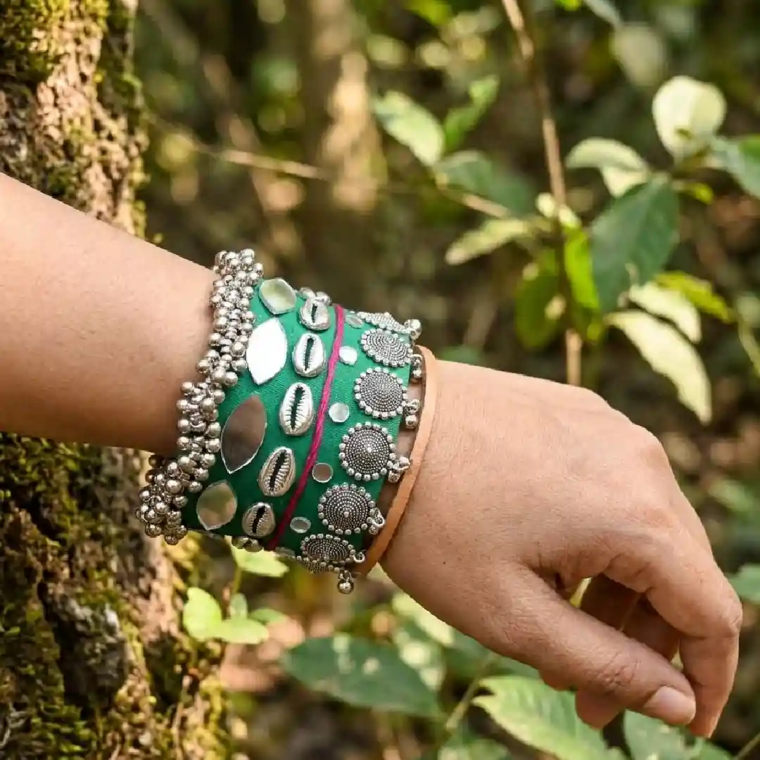Model wearing a single handcrafted green fabric wide cuff with mirror work and cowrie shells against a natural forest background