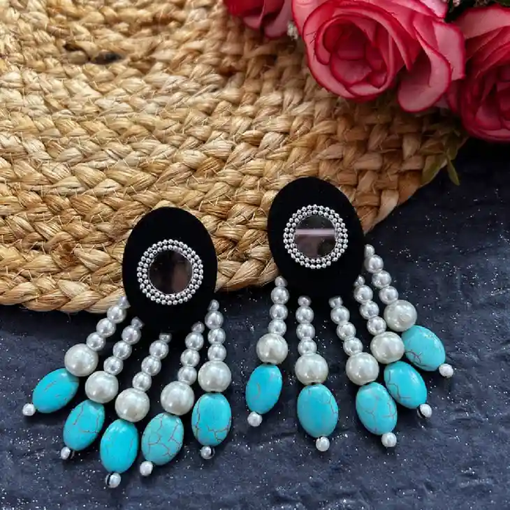handcrafted dangler earrings with multiple pearl strands and clustered turquoise beads, set against a blurred background of colorful stalls and warm string lights.