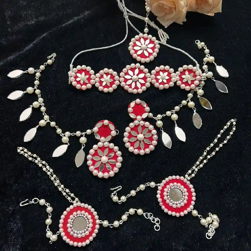 A complete handcrafted red fabric jewelry set with white pearl borders and floral mirror work designs, featuring a choker, drop earrings, maangtika, and matching haathphools on a black background.