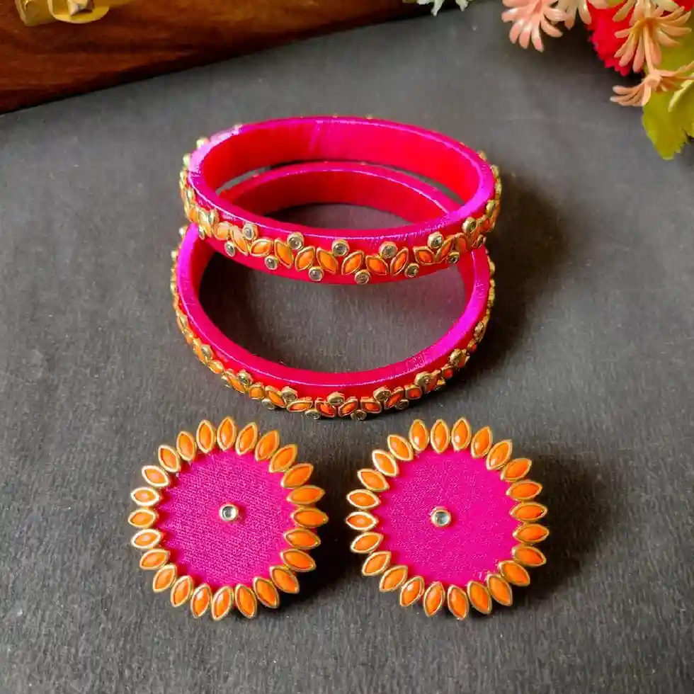 Handcrafted hot pink silk thread bangles and matching large circular stud earrings with orange kundan stone borders on a dark grey background.