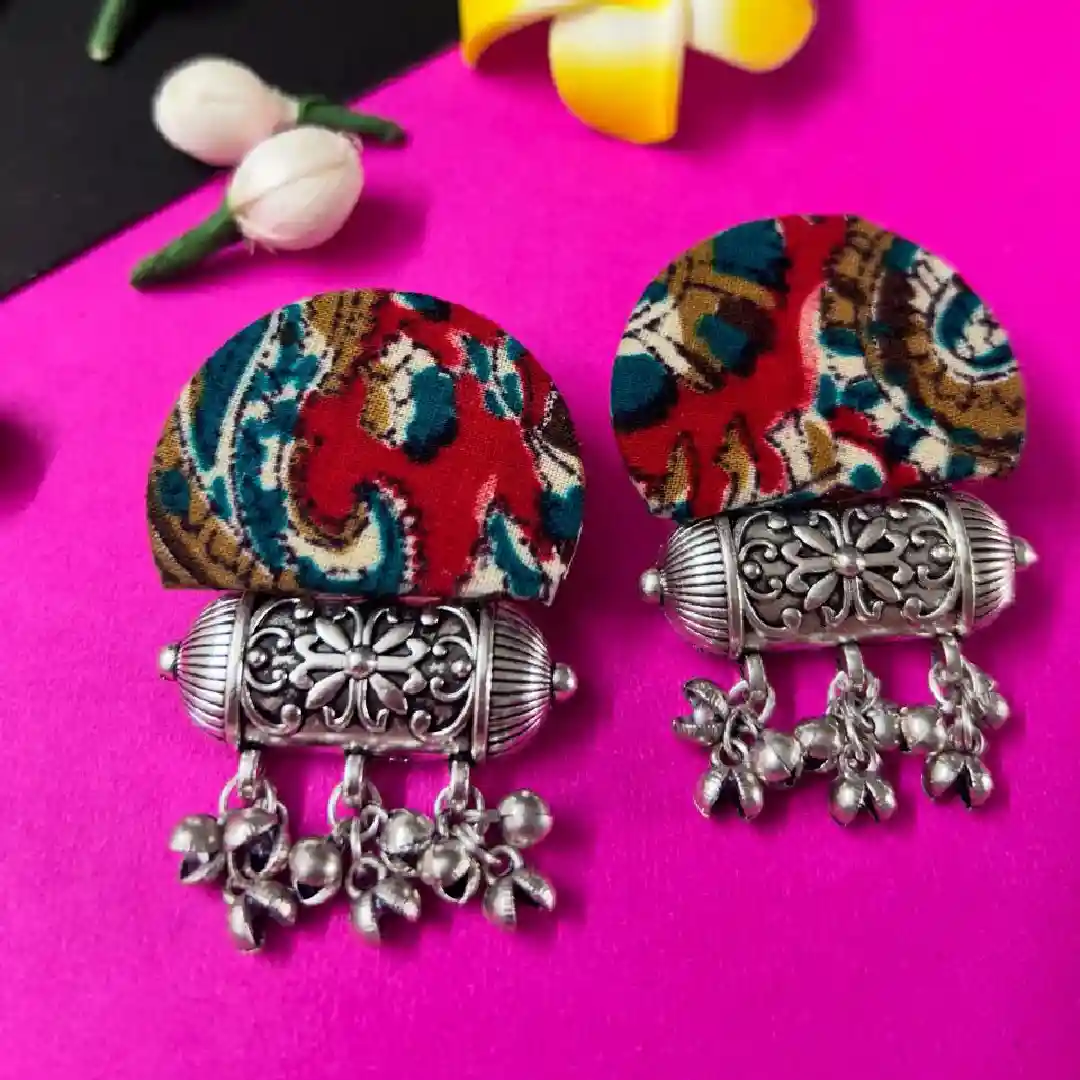 Pair of traditional earrings featuring red and teal Kalamkari fabric studs with intricate oxidized silver floral pendants and hanging ghungroo bells.