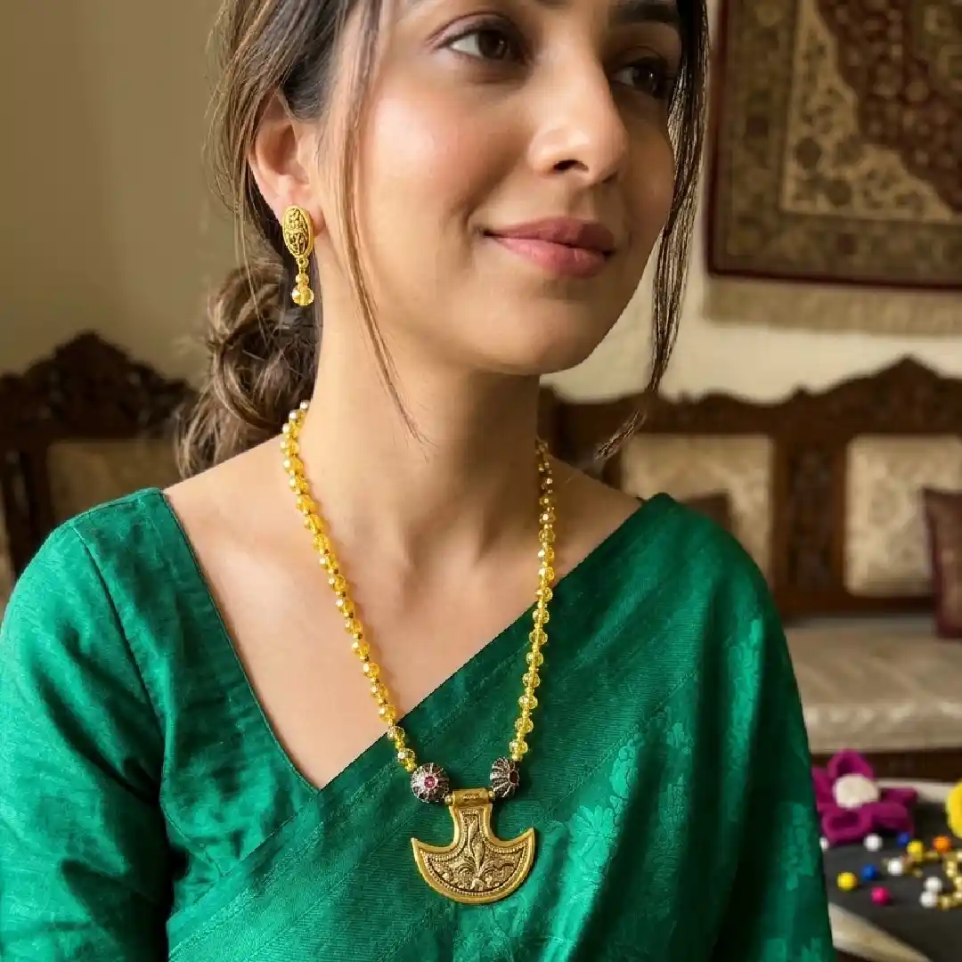 A model wearing an antique gold-toned crescent pendant necklace with yellow crystal beads, paired with a royal purple silk saree for a striking contrast.