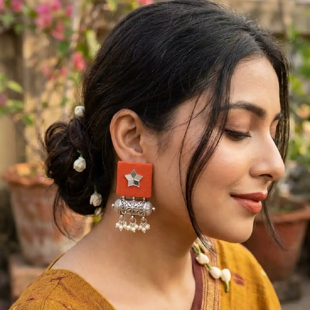 An elegant woman showcasing handcrafted orange square fabric earrings with a star-shaped mirror and silver oxidized dholki beads for itsybitsykolkata.com.