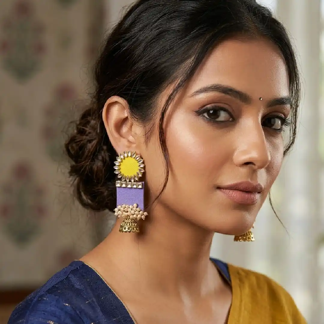 Elegant woman in lilac ethnic wear showcasing handcrafted fabric jhumka earrings with yellow Kundan studs and white pearl clusters.