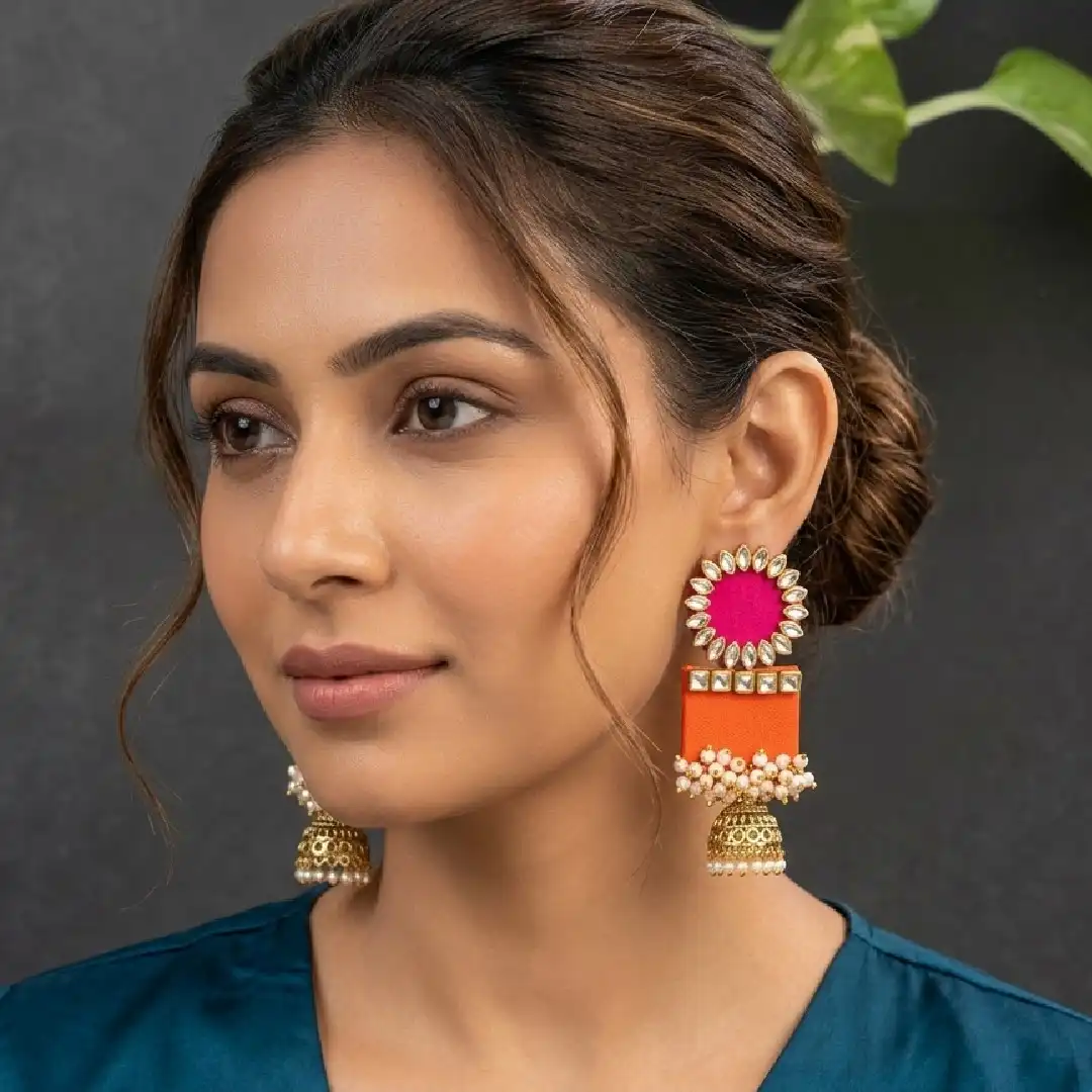 A model elegantly showcasing handcrafted pink and orange fabric jhumka earrings featuring white Kundan stone studs and pearl bead clusters.