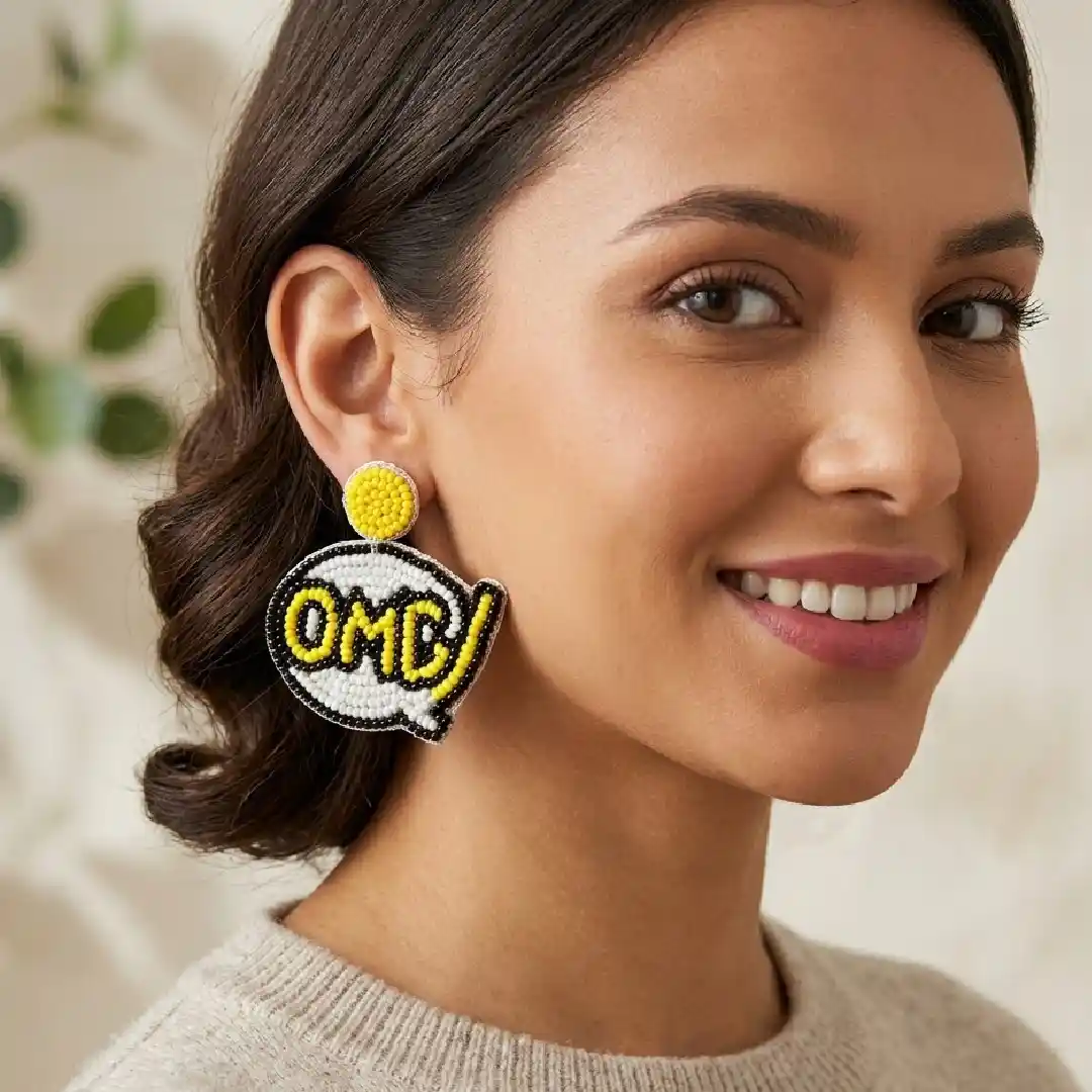 A model wearing handcrafted 'OMG' speech bubble statement earrings made with yellow, white, and black seed beads, styled with a casual beige sweater.