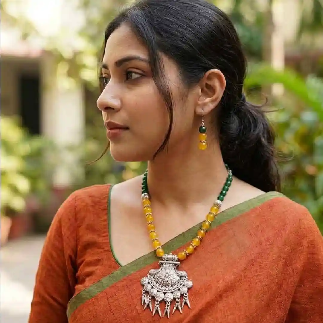  Lifestyle model shot for Itsy Bitsy Kolkata featuring a woman in an ivory cotton saree wearing a handcrafted tribal oxidized silver necklace with yellow and forest green onyx beads and matching drop earrings.
