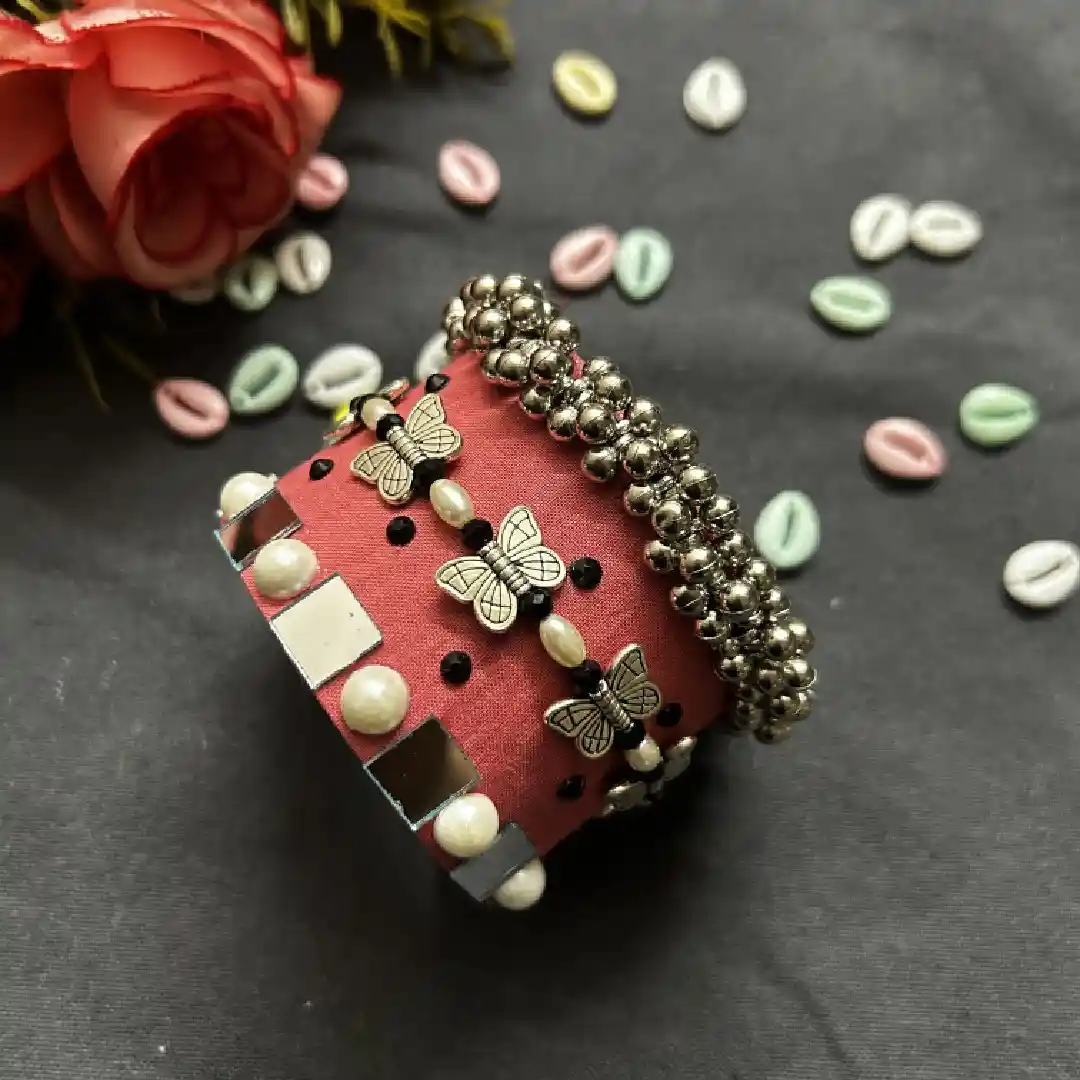 Handcrafted peach fabric cuff bracelet by Itsy Bitzy Kolkata featuring silver-toned butterfly charms, delicate white pearls, and reflective mirror work embellishments.
