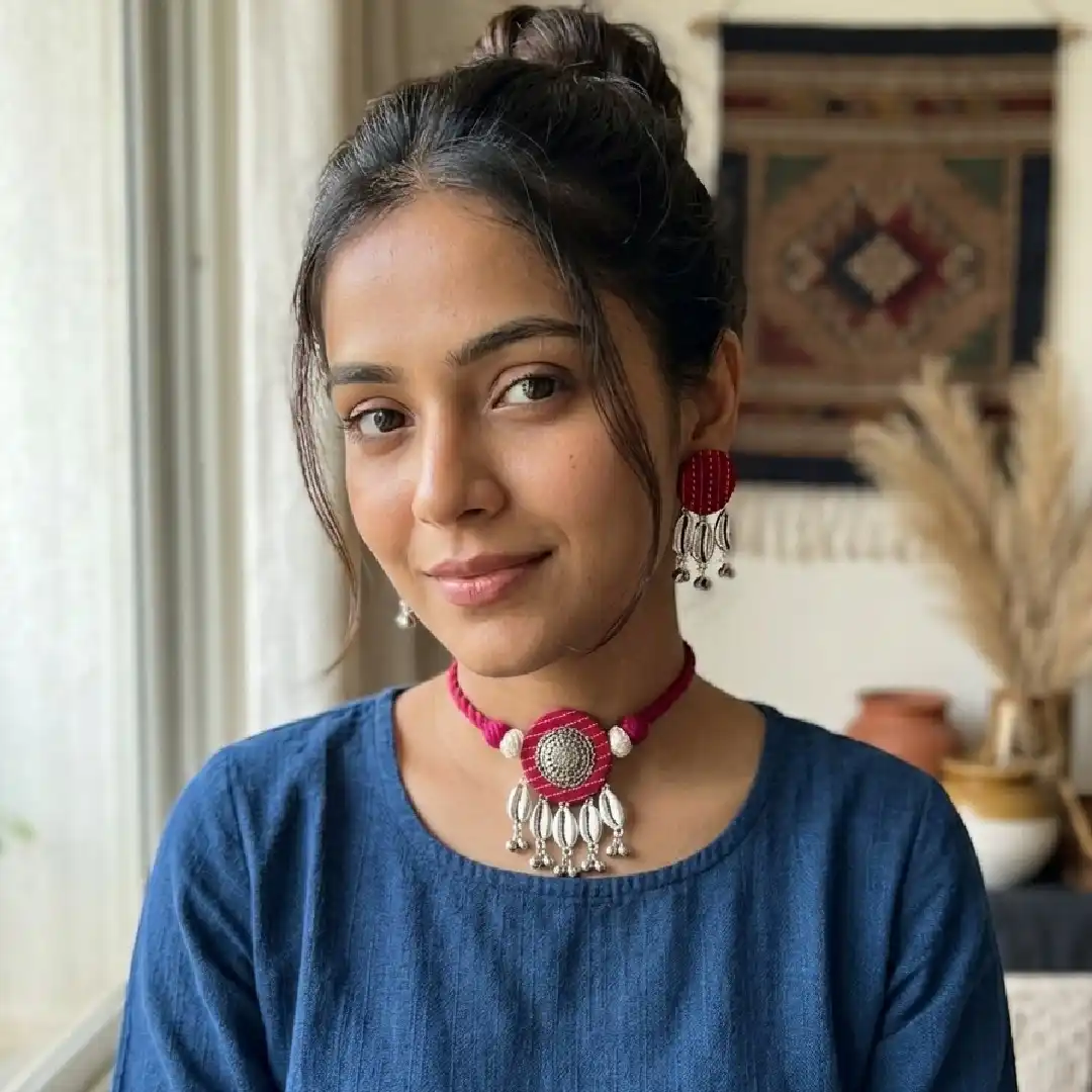 Model showcasing a handcrafted rani pink fabric choker and earring set from Itsy Bitzy Kolkata, featuring oxidised silver accents and shell charms, styled with a simple blue cotton kurta.