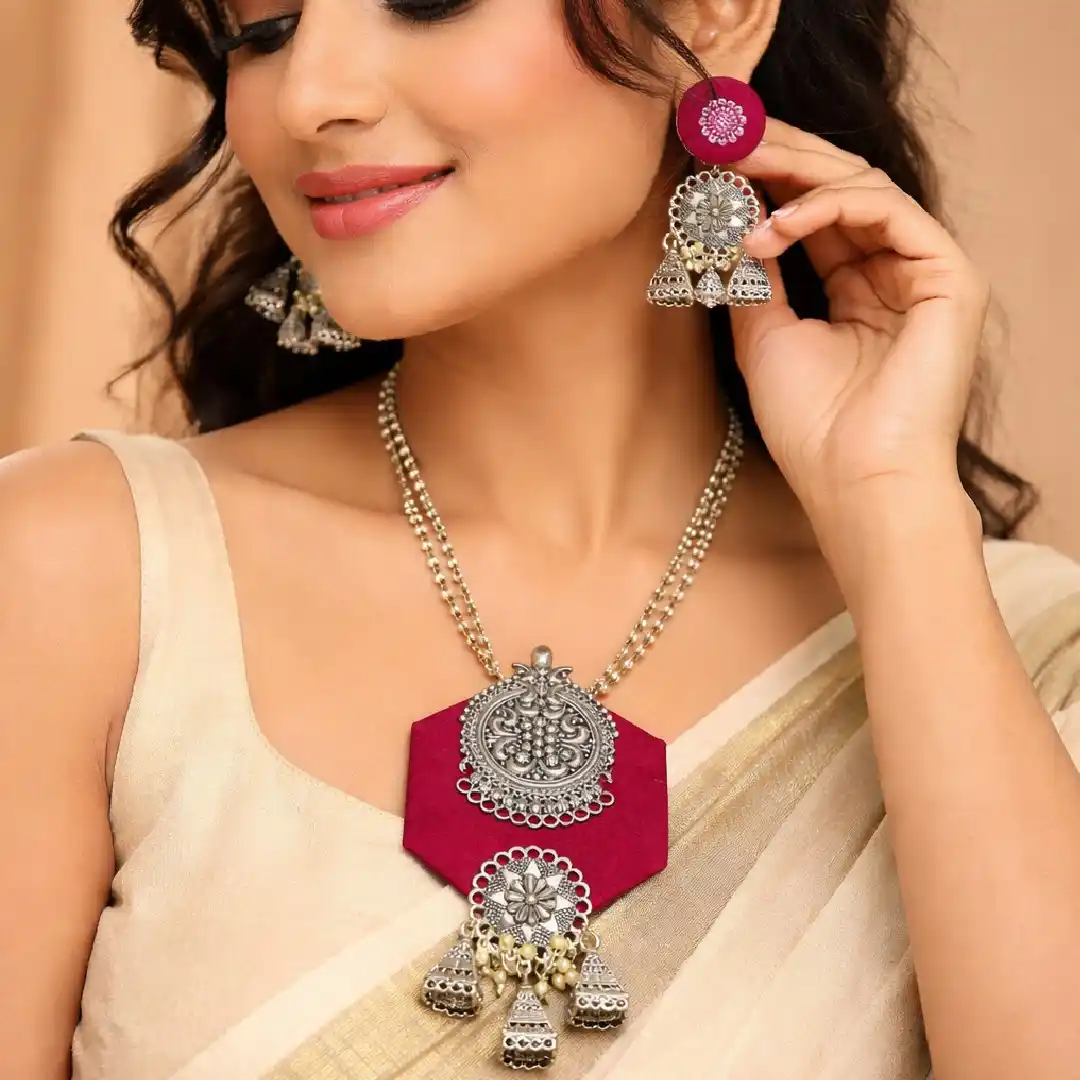 Woman wearing rani pink fabric oxidised silver necklace set with statement pendant and matching earrings styled with cream saree for festive and ethnic look