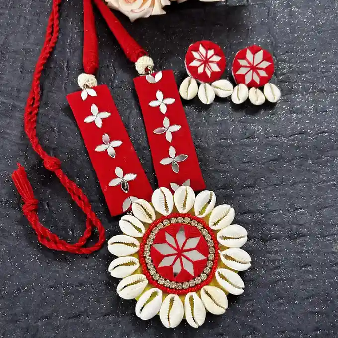 Handcrafted red fabric jewelry set by Itsy Bitzy Kolkata featuring a long pendant necklace and matching earrings adorned with white cowrie shells and floral mirror work patterns.