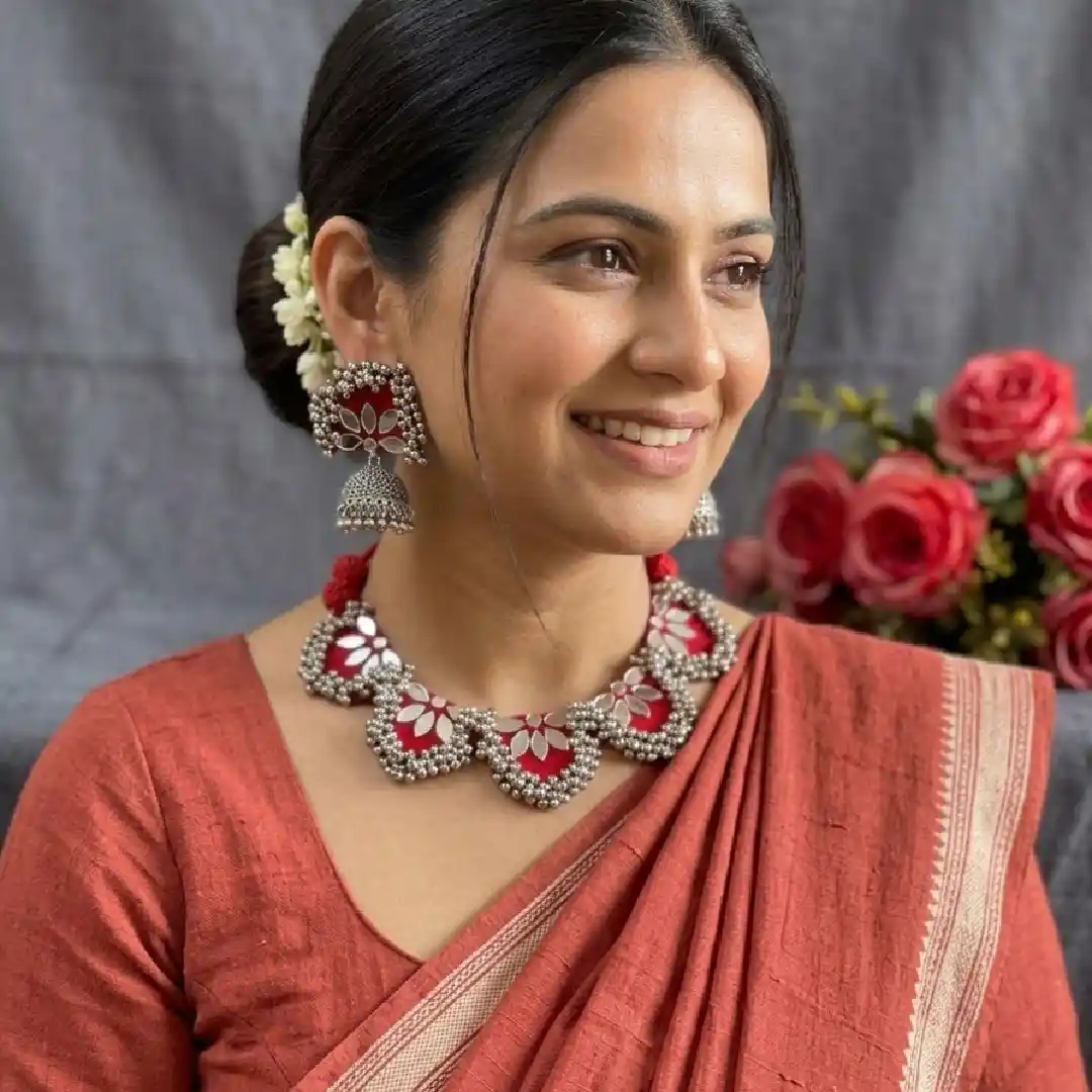 Model elegantly styled in a terracotta cotton saree, wearing a handcrafted red fabric choker with floral mirror work and matching silver jhumka earrings from Itsy Bitsy Kolkata.