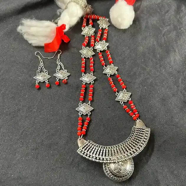 Traditional silver-plated oxidized necklace featuring red beads and a detailed floral tribal pendant with matching earrings.