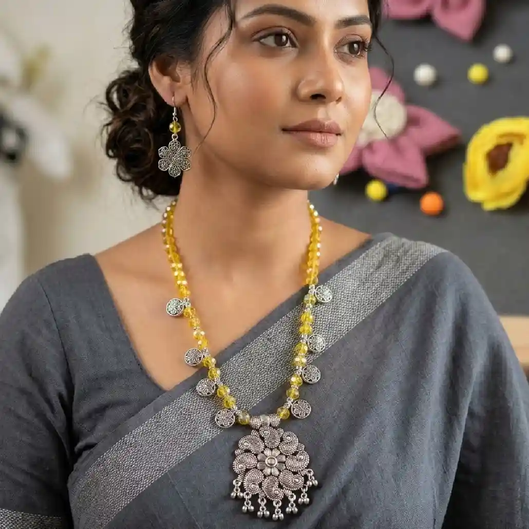 Lifestyle shot of a model wearing the handcrafted yellow crystal bead necklace and paisley pendant set by Itsy Bitsy Kolkata, styled with a crisp white cotton saree on a sunlit ethnic balcony.