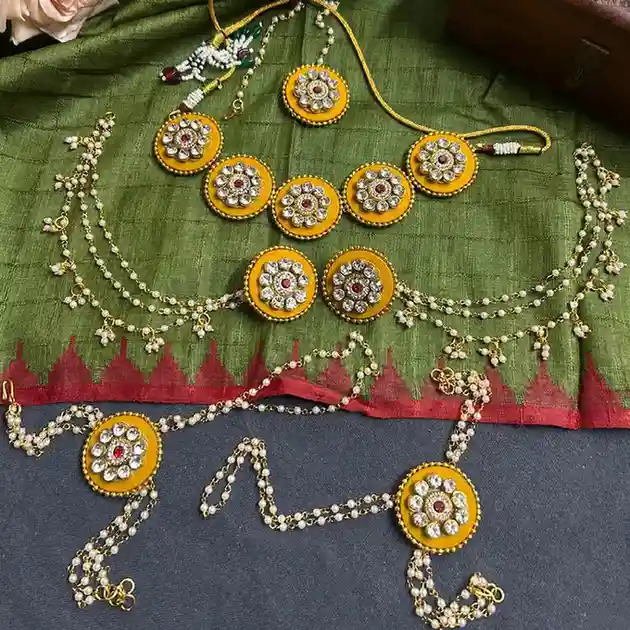 A complete yellow fabric and Kundan jewelry set with pearl chains displayed on green ethnic fabric, perfect for Haldi ceremonies.